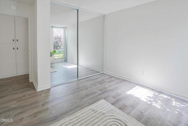 unfurnished bedroom with wood finished floors, a closet, baseboards, and a textured ceiling