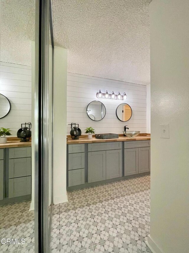 detailed view of tile patterned floors, vanity, wood walls, and a textured ceiling