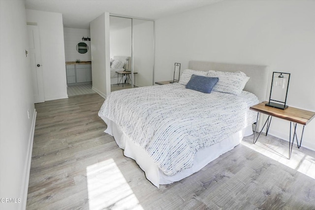 bedroom featuring light wood finished floors, baseboards, a closet, and connected bathroom