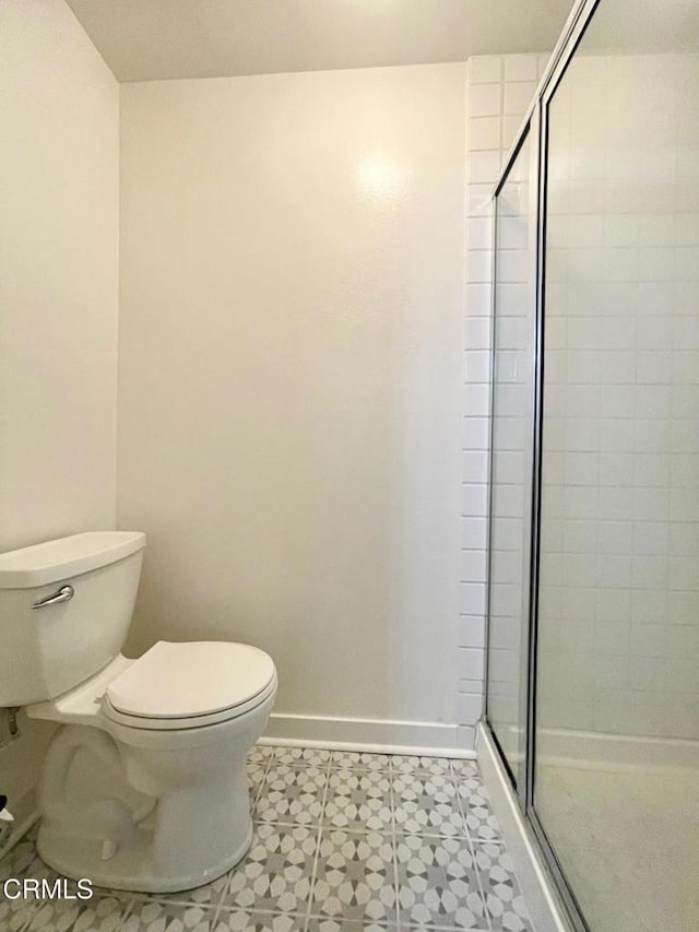 bathroom with toilet, a stall shower, baseboards, and tile patterned floors