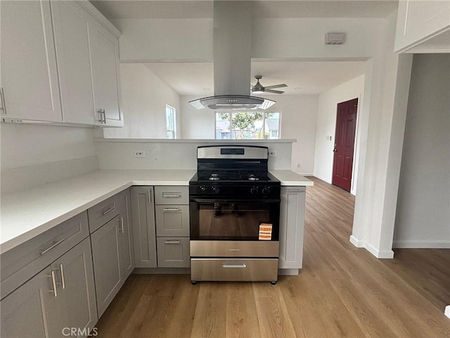 kitchen with gas stove, island range hood, a peninsula, gray cabinetry, and ceiling fan