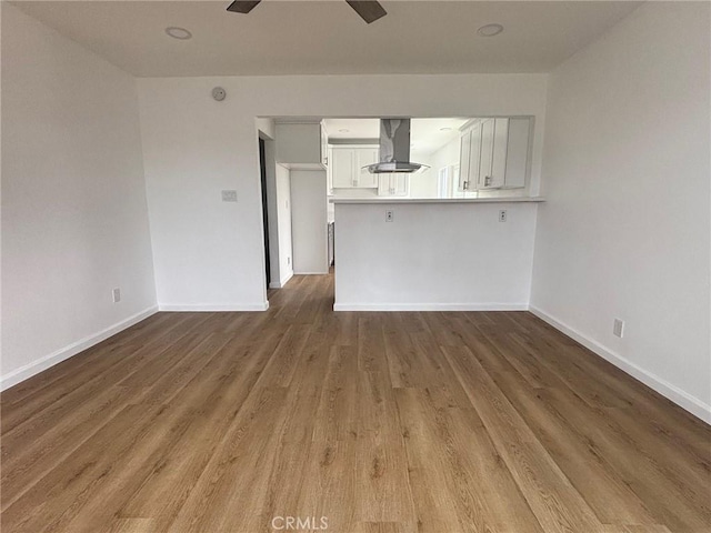 unfurnished living room featuring a ceiling fan, wood finished floors, and baseboards