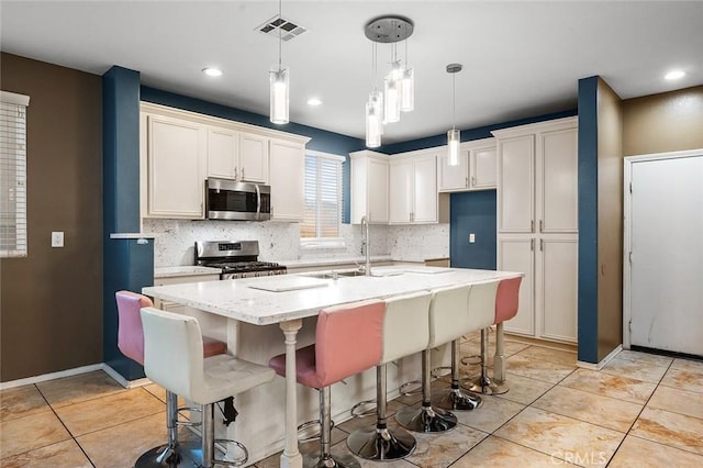 14271 Blackstone St, Hesperia, CA 92345 - kitchen with stainless steel appliances, tasteful backsplash, a kitchen island with sink, light tile patterned floors, and light stone countertops