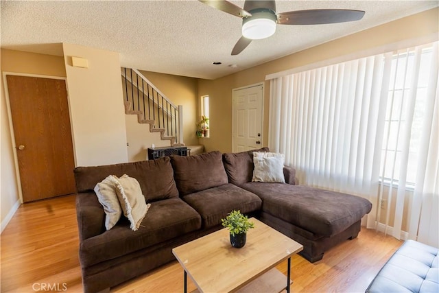 living area featuring light wood-style flooring, baseboards, ceiling fan, stairs, and a textured ceiling