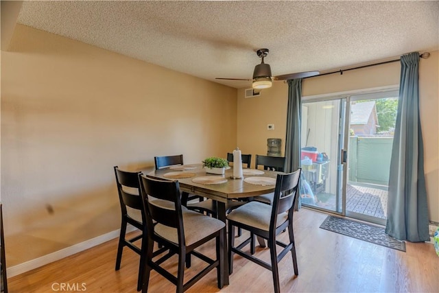 dining space featuring light wood-style floors, a textured ceiling, baseboards, and ceiling fan