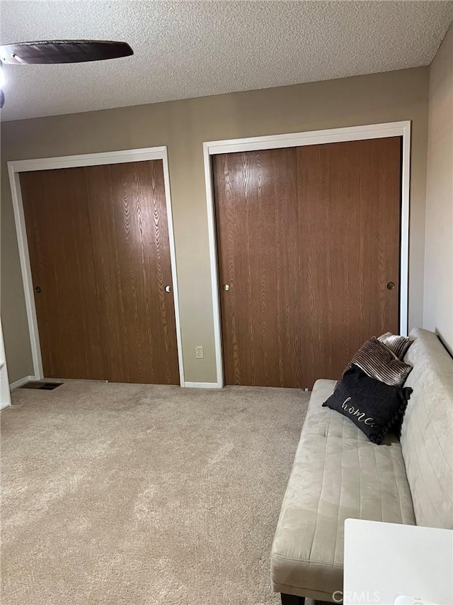 carpeted bedroom with multiple closets, ceiling fan, and a textured ceiling