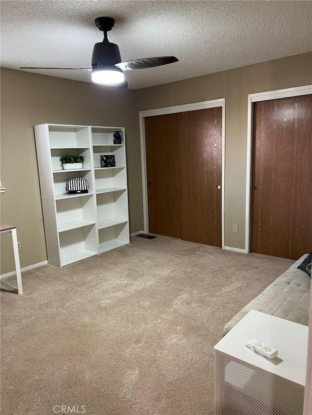 unfurnished bedroom featuring carpet flooring, two closets, a ceiling fan, a textured ceiling, and baseboards
