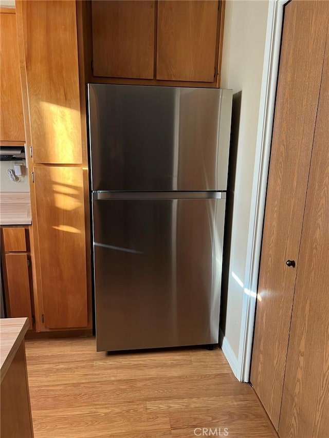 kitchen view of freestanding refrigerator, light countertops, light wood-type flooring, and brown cabinets