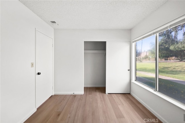 unfurnished bedroom featuring light wood-style flooring, a textured ceiling, a closet, and baseboards