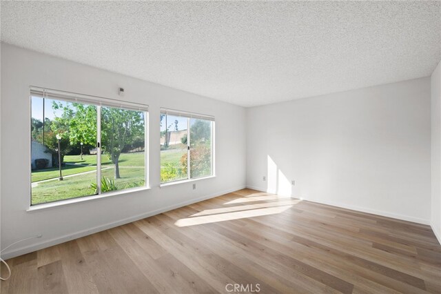 spare room with wood finished floors, a textured ceiling, and baseboards