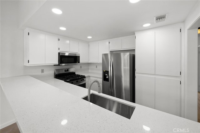 kitchen with appliances with stainless steel finishes, a sink, white cabinetry, recessed lighting, and light stone counters