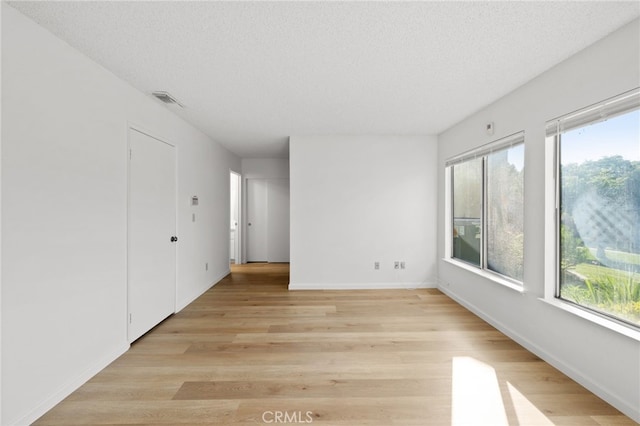 unfurnished room with plenty of natural light, light wood-type flooring, baseboards, and a textured ceiling