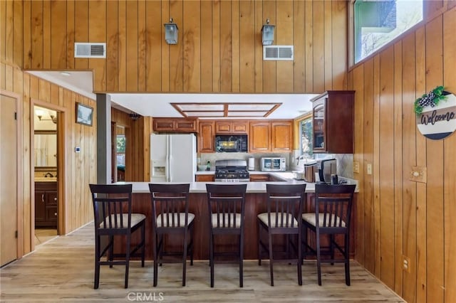 24514 Albrun Dr, Crestline, CA 92325 - kitchen with white refrigerator with ice dispenser, black microwave, gas stove, wood walls, and light wood-style floors