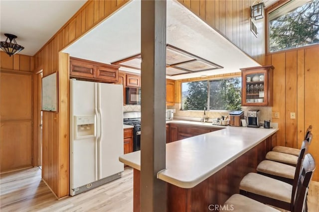 24514 Albrun Dr, Crestline, CA 92325 - kitchen featuring white refrigerator with ice dispenser, black microwave, wooden walls, brown cabinetry, and light wood-style floors