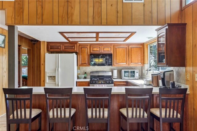 24514 Albrun Dr, Crestline, CA 92325 - kitchen featuring white fridge with ice dispenser, stainless steel range with gas cooktop, black microwave, light countertops, and decorative backsplash