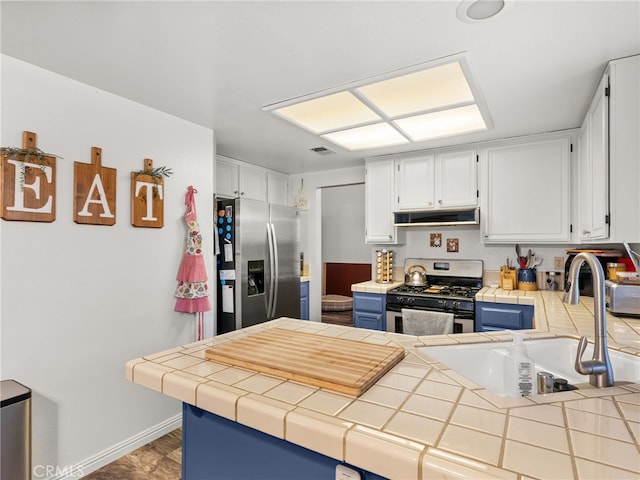 kitchen featuring appliances with stainless steel finishes, a sink, white cabinets, under cabinet range hood, and tile countertops