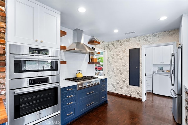 2618 N Louise St, Santa Ana, CA 92706 - kitchen with washer / dryer, blue cabinetry, wallpapered walls, stainless steel appliances, and wall chimney exhaust hood