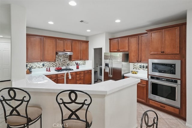 29661 Cambridge Ave, Castaic, CA 91384 - kitchen featuring appliances with stainless steel finishes, under cabinet range hood, backsplash, a peninsula, and brown cabinetry
