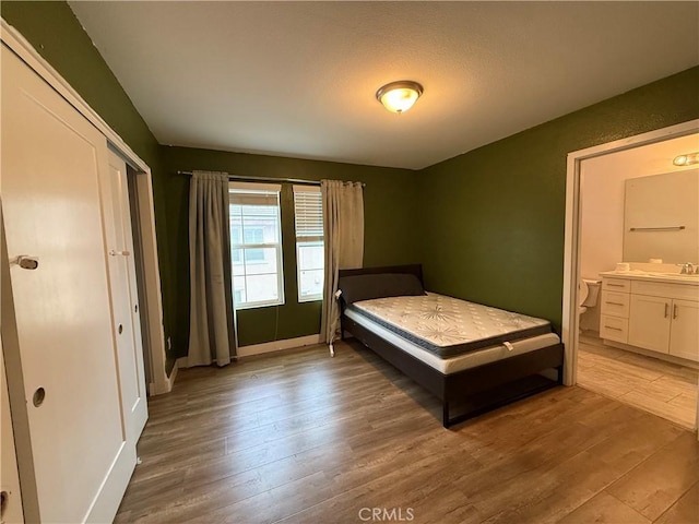 bedroom featuring a sink, wood finished floors, baseboards, and ensuite bathroom