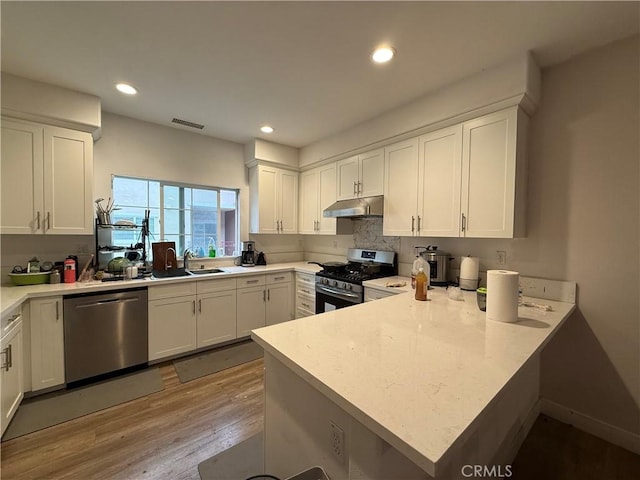 kitchen with appliances with stainless steel finishes, under cabinet range hood, a peninsula, light wood-style floors, and white cabinets