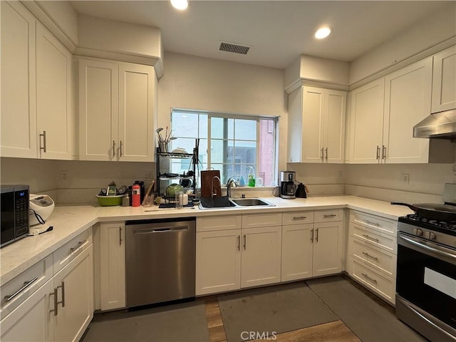 kitchen featuring stainless steel appliances, a sink, white cabinetry, under cabinet range hood, and recessed lighting