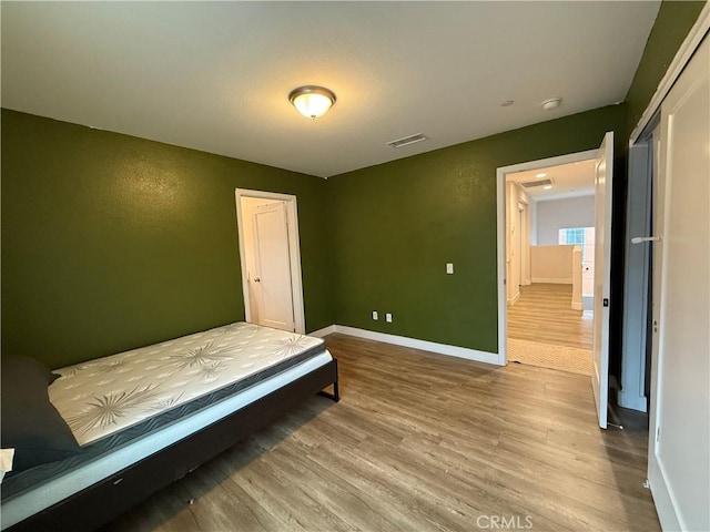 bedroom with wood finished floors, baseboards, and a closet