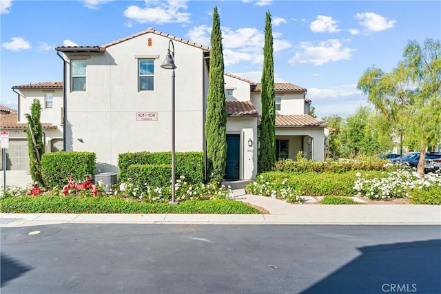 mediterranean / spanish-style house with a tiled roof, stucco siding, central AC, and a garage