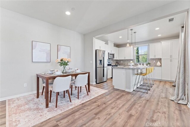 kitchen featuring stainless steel appliances, a breakfast bar, light wood finished floors, white cabinets, and decorative backsplash