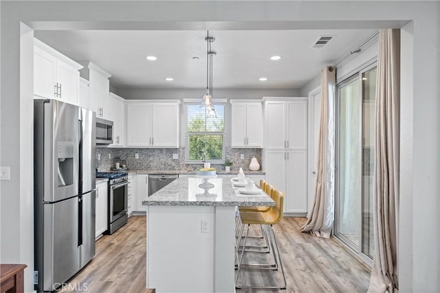 kitchen with stainless steel appliances, light wood-type flooring, white cabinets, a kitchen island, and tasteful backsplash
