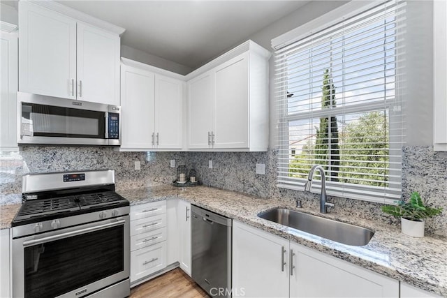 kitchen with stainless steel appliances, a sink, white cabinetry, tasteful backsplash, and light stone countertops