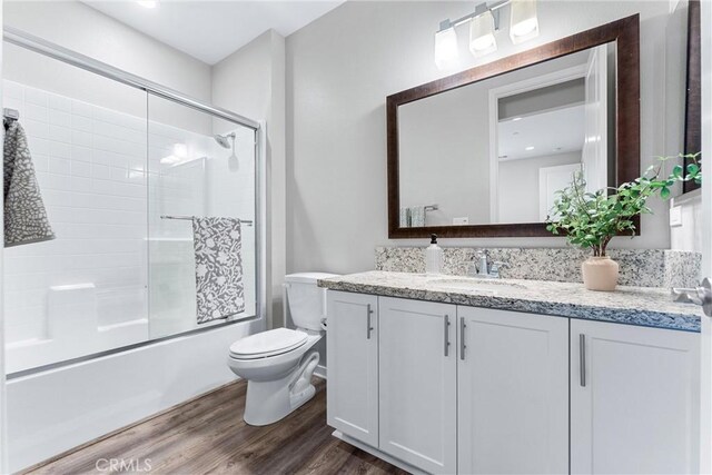 full bath featuring toilet, wood finished floors, vanity, and shower / bath combination with glass door