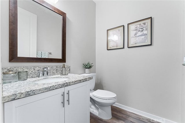 half bathroom featuring wood finished floors, vanity, baseboards, and toilet