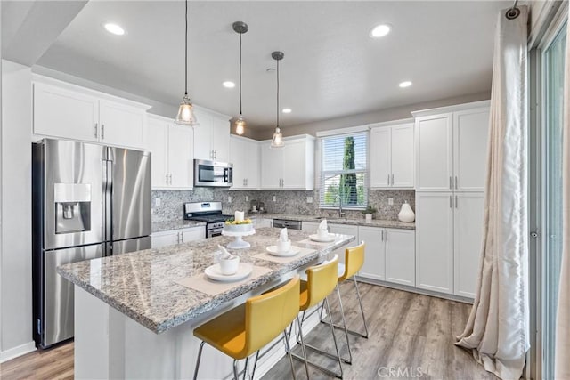 kitchen featuring appliances with stainless steel finishes, a sink, light wood-style flooring, white cabinetry, and a center island