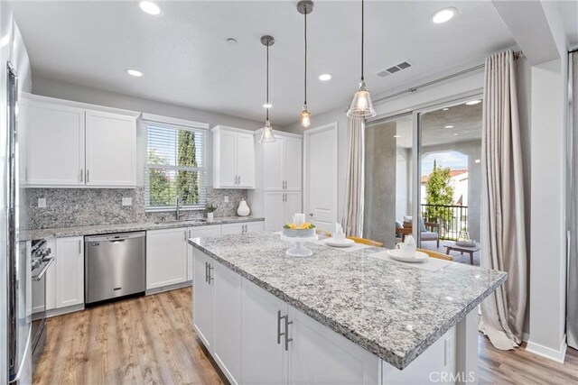 kitchen featuring dishwasher, light wood finished floors, white cabinetry, a center island, and backsplash