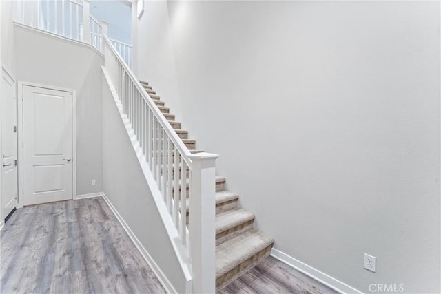 staircase featuring baseboards, wood finished floors, and a high ceiling