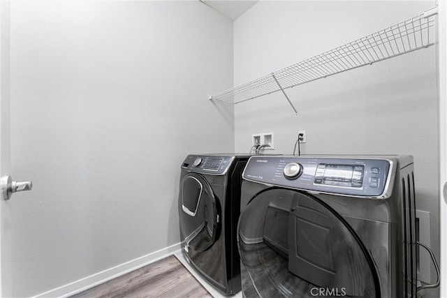 clothes washing area featuring separate washer and dryer, baseboards, and wood finished floors