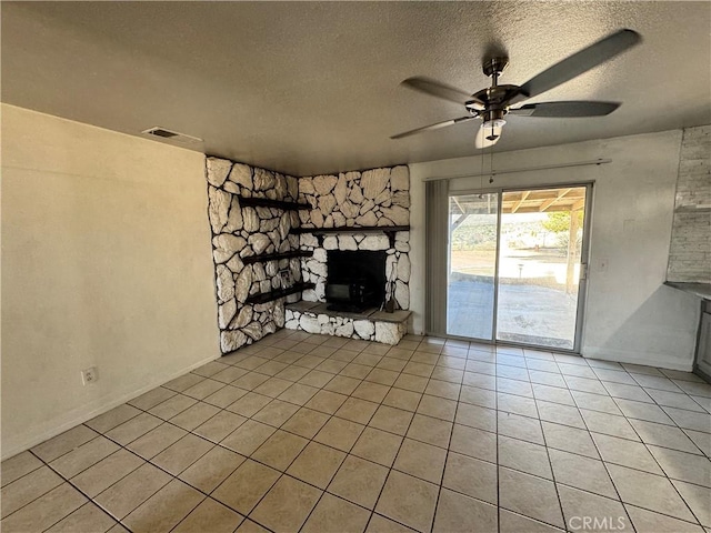 8723 Palomar Ave, Yucca Valley, CA 92284 - unfurnished living room with a stone fireplace, a textured ceiling, light tile patterned flooring, and a ceiling fan