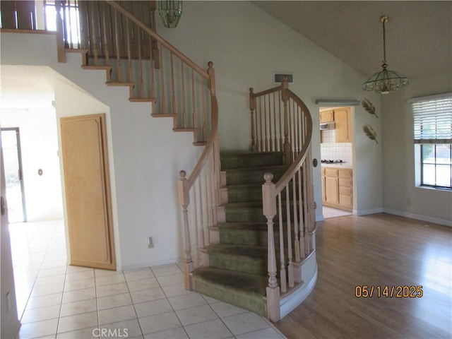 stairs with high vaulted ceiling, wood finished floors, baseboards, and a chandelier