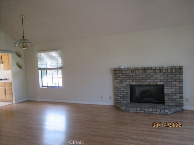 unfurnished living room with wood finished floors, baseboards, vaulted ceiling, and a brick fireplace
