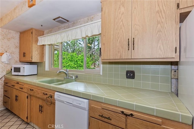 kitchen featuring white appliances, a sink, decorative backsplash, wallpapered walls, and tile counters