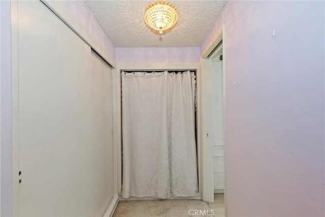 corridor with a textured ceiling and light colored carpet