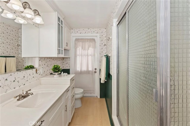 bathroom featuring wallpapered walls, wood finished floors, a stall shower, vanity, and toilet