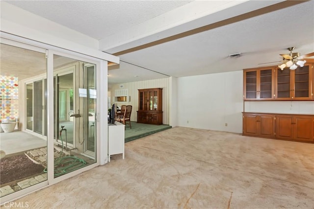 empty room featuring light colored carpet, a textured ceiling, ceiling fan, and beam ceiling
