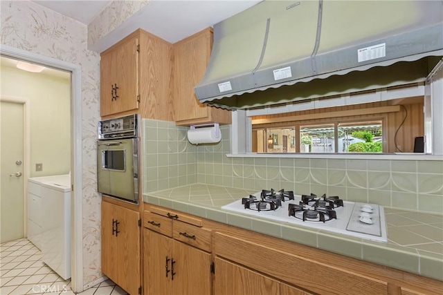 kitchen with wall oven, tile countertops, under cabinet range hood, decorative backsplash, and wallpapered walls
