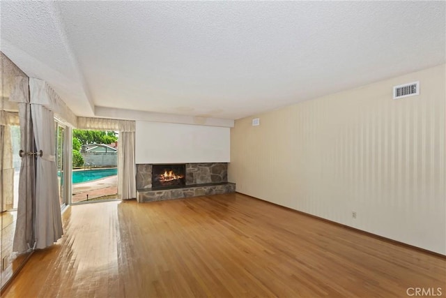 unfurnished living room featuring wood finished floors, a stone fireplace, and a textured ceiling