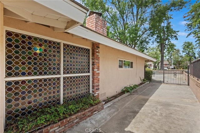 view of home's exterior featuring a chimney, stucco siding, and a gate