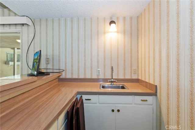 kitchen with wallpapered walls, a sink, a textured ceiling, and white cabinetry