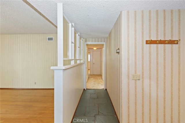 corridor featuring a textured ceiling and wallpapered walls
