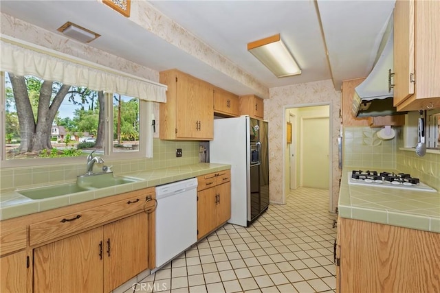 kitchen with white appliances, a sink, tile counters, backsplash, and exhaust hood