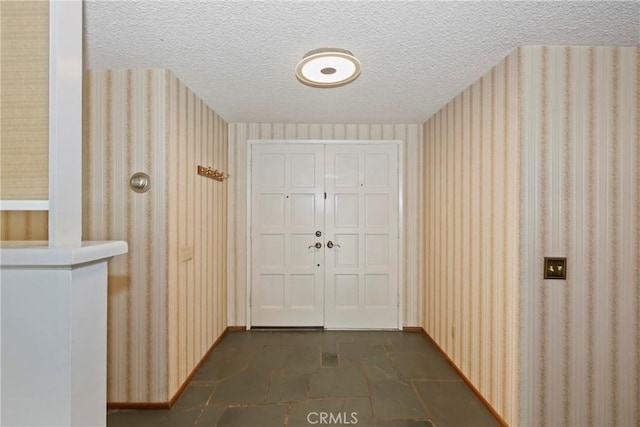 entryway featuring wallpapered walls, a textured ceiling, and baseboards